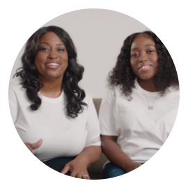 A mother and daughter sitting next to each other smiling.